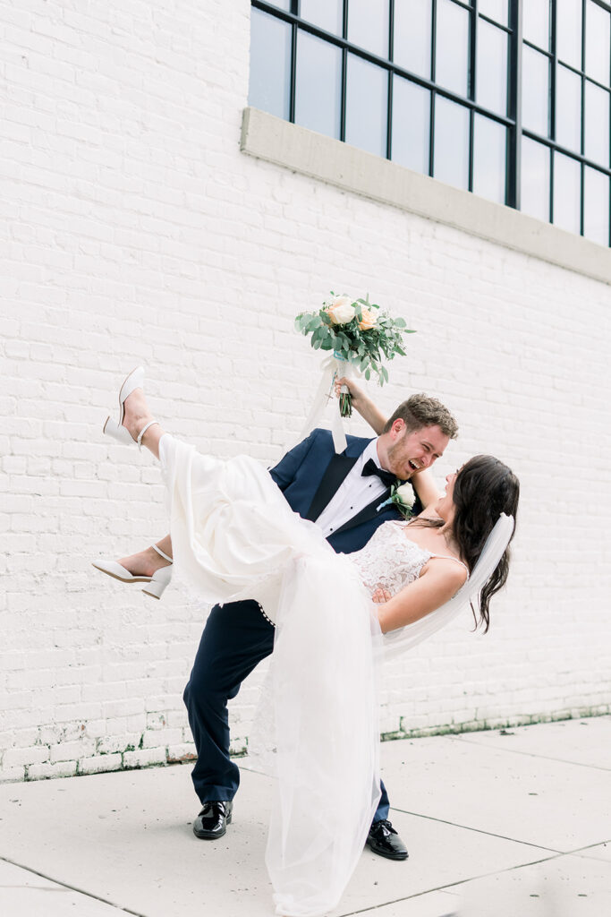 Groom dips bride while holding her. Bride holds bouquet behind grooms head. Captured in front of Baltimore wedding venues