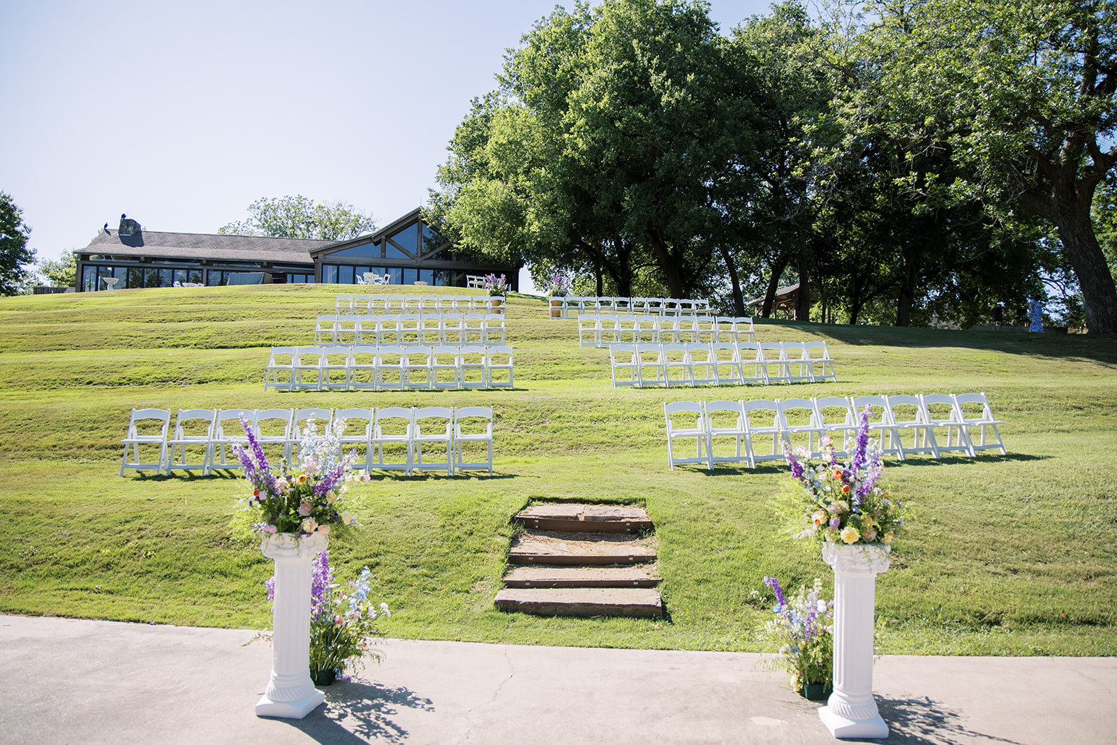 Spring Austin wedding with flowers on the sides of alter with white chairs along green grass.