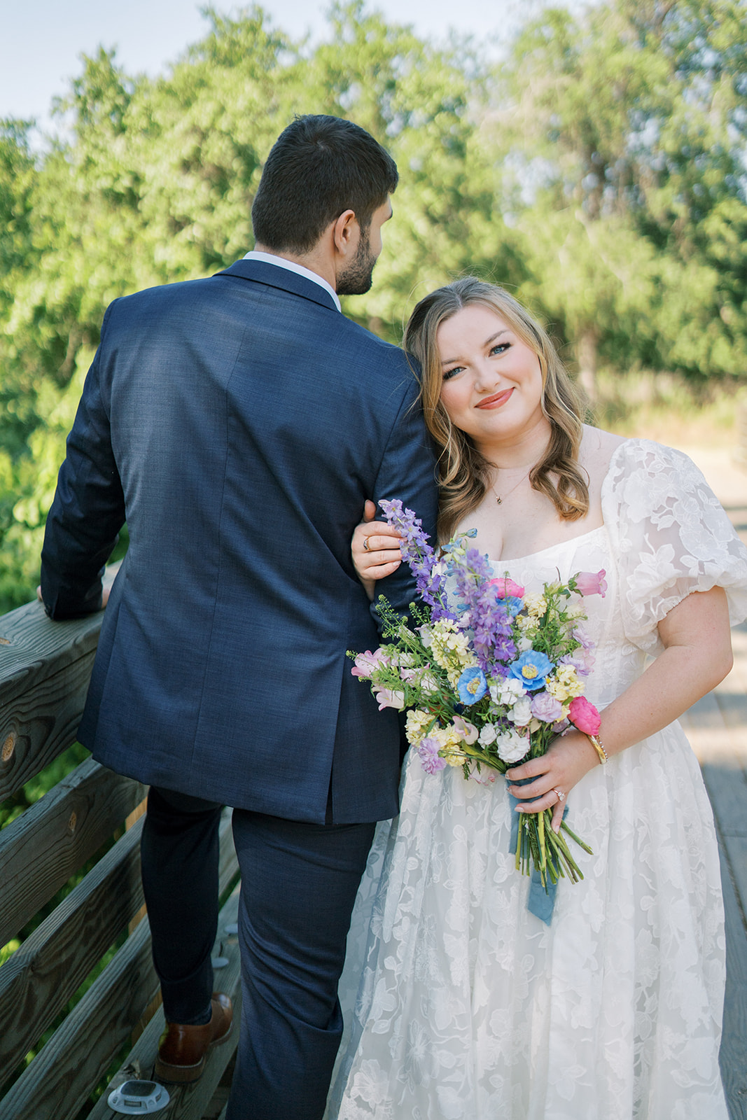 Groom faces away from the camera. Bride holds his arm and looks at the camera smiling. Captured by Austin wedding photographer