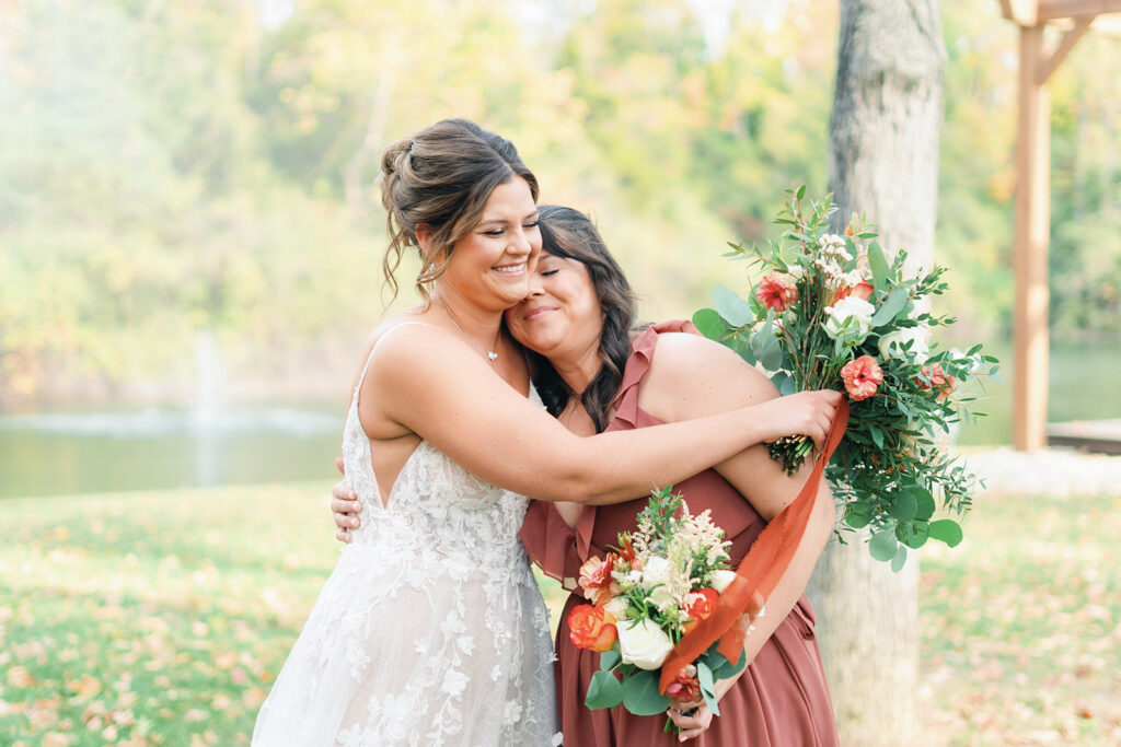 Bride in white lacey dress hugs mother carrying bouquets of orange and white flowers in a mauve dress taken by Baltimore wedding photographer